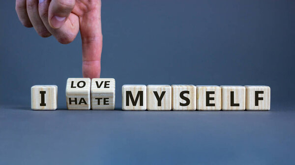 Hand turns cubes and changes the expression 'I hate myself' to 'I love myself'. Beautiful grey background, copy space. Concept.