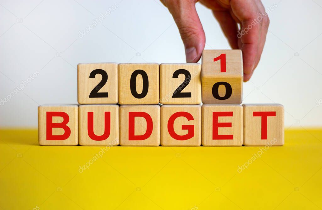 Business concept of planning 2021. Male hand flips wooden cube and change the inscription 'BUDGET 2020' to 'BUDGET 2021'. Beautiful yellow table, white background, copy space.