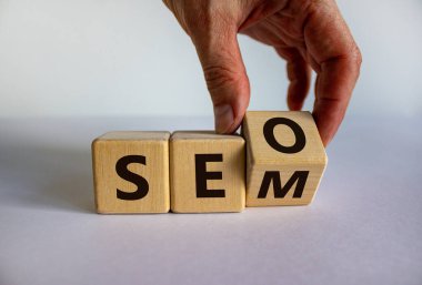 SEO SEM 'e karşı. Erkek eli küpü çevirir ve 'SEO' ifadesini 'SEM' ya çevirir ya da tam tersi. SEO ve SEM veya Arama Motoru optimizasyonu ve Arama Motoru Matketing için kavram. Güzel beyaz arkaplan, kopyalama alanı.