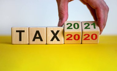 İş planı 2021. Erkek eli ahşap küpü çevirir ve 'vergi 2020' yazısını 'vergi 2021' olarak değiştirir. Güzel sarı masa, beyaz arkaplan, kopyalama alanı.