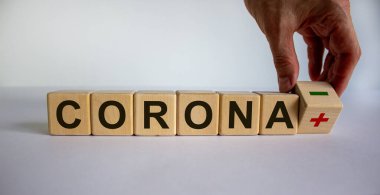 Negatif korona testinin sembolü. Erkek el küpü çevirir ve 'corona artı' corona eksi 'ifadesini değiştirir. Güzel beyaz arka plan. İş konsepti. Boşluğu kopyala.