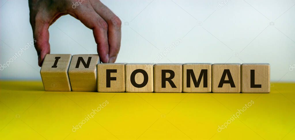 Male hand flips wooden cubes and change the inscription 'formal' to 'informal'. Beautiful yellow table, white background, copy space.