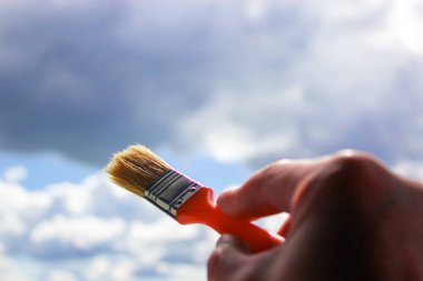 Boyayı gökyüzüne doğru tutarken yakın plan. Bulutlar boyuyor. Kavram. Güneş ışığı ve bulutlar.