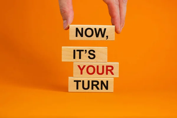 Wooden blocks form the words \'now, it\'s your turn\' on beautiful orange background. Male hand. Beautiful background. Business concept.