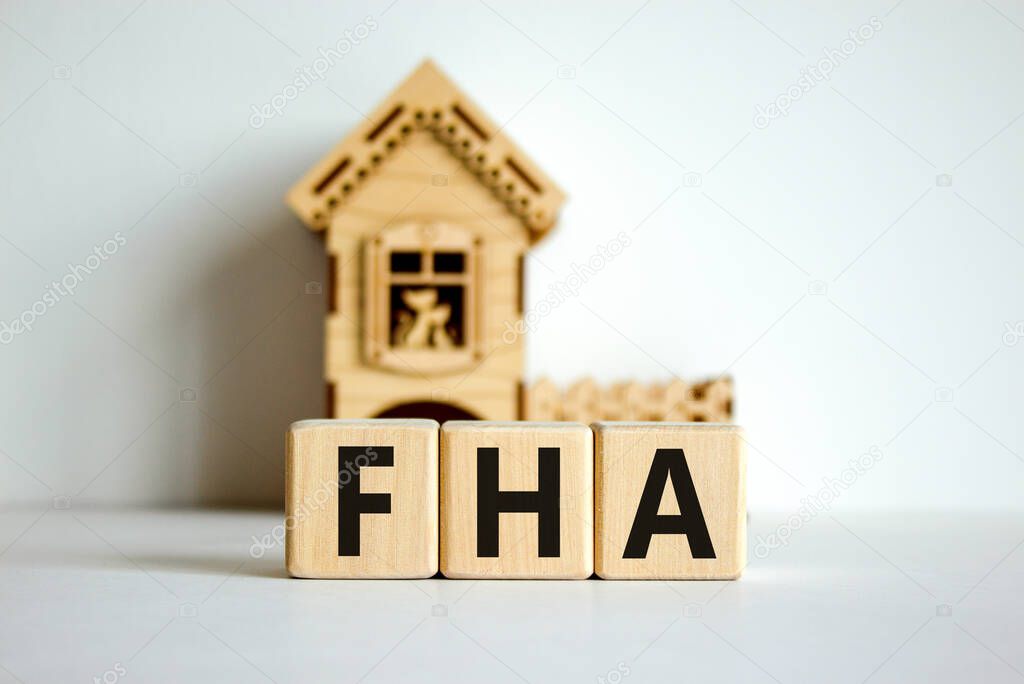 Wooden cubes form the word 'FHA, federal housing administration' near miniature house. Beautiful white background, copy space. business concept.