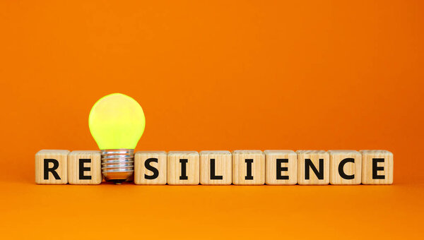 Wooden cubes with word 'resilience'. Yellow light bulb. Beautiful orange background. Business concept. Copy space.
