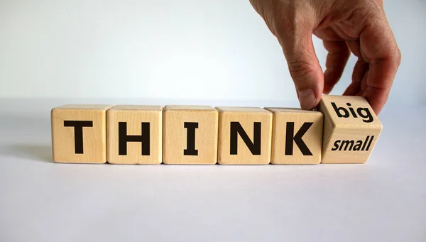 Think small or think big. Hand flips a cube and changes the words \'think small\' to \'think big\' or vice versa. Beautiful white background. Business concept. Copy space.