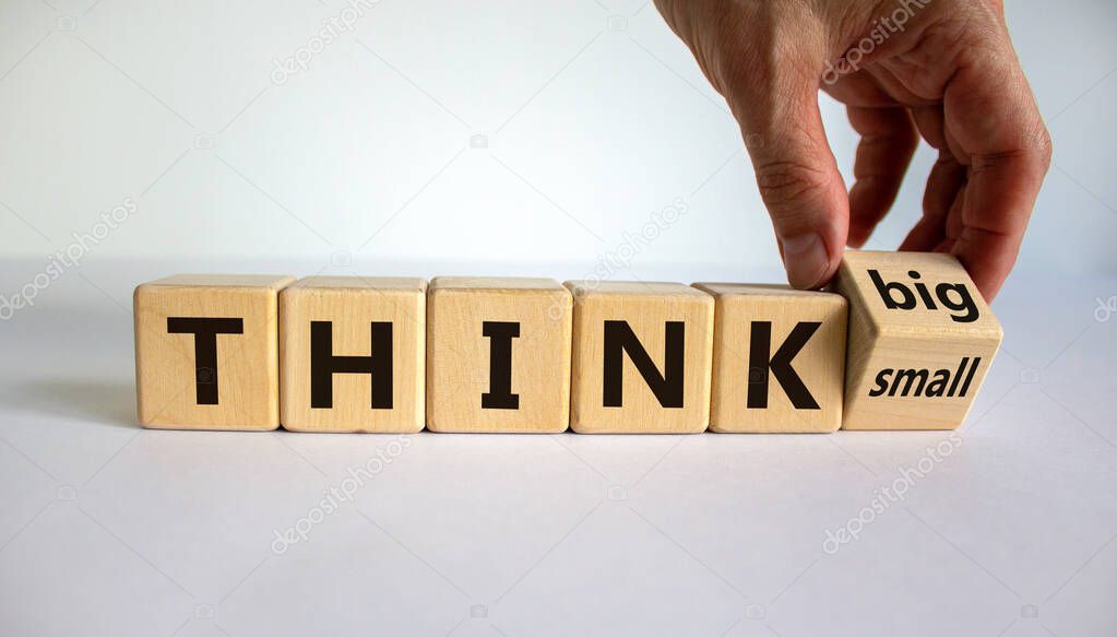 Think small or think big. Hand flips a cube and changes the words 'think small' to 'think big' or vice versa. Beautiful white background. Business concept. Copy space.