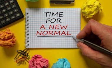 Beyaz nota, güzel sarı arkaplana, renkli ataçlara, metal kaleme, kapağa ve hesap makinesine yeni bir normal yazma zamanı. İş konsepti.