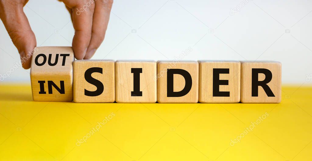 Hand turns a cube and changes the expression 'insider' to 'outsider' or vice versa. Beautiful yellow table, white background.  Copy space.