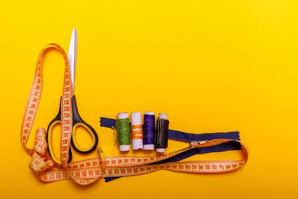 Flat lay of colored thread rolls and Scissors for sewing yellow background. Sewing and needlework concept. Tools for sewing and handmade: thread, scissors.