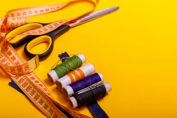 Flat lay of colored thread rolls and Scissors for sewing yellow background. Sewing and needlework concept. Tools for sewing and handmade: thread, scissors.