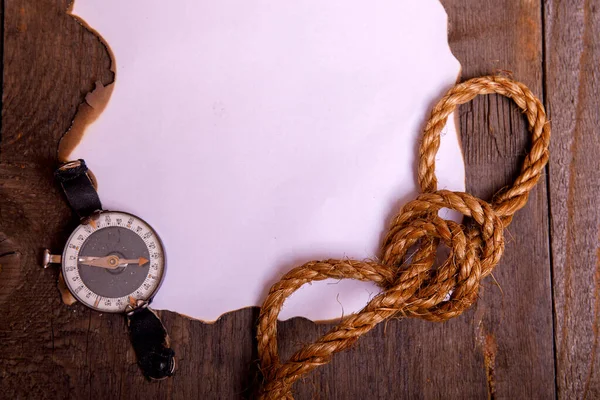 Old paper with compass, knife and rope on vintage wooden table. Top view of empty space for your text.