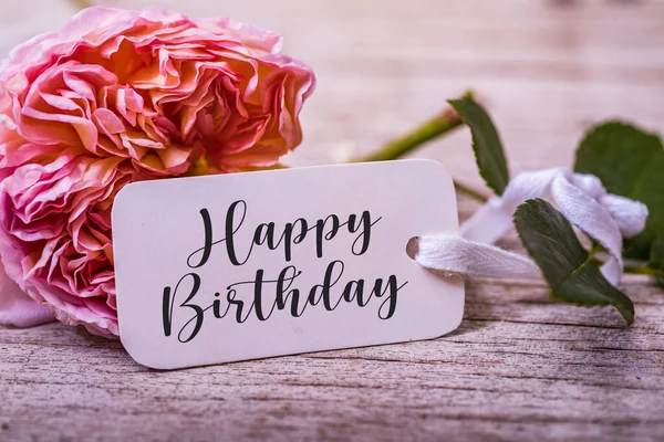 Birthday background with flowers and card. Rose and happy birthday word on white card. Pastel colors on selective focus image.