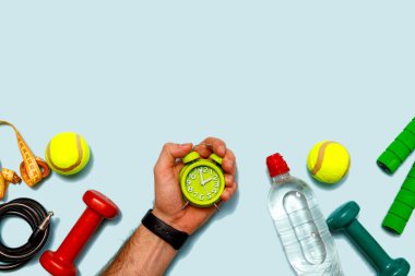 Yeşil alarm saati, tenis topu, bir şişe su, mezura, erkek eli ve halterden oluşan düz bir atış. Metin için kopyalama alanı olan üst görünüm. Fitness konsepti.