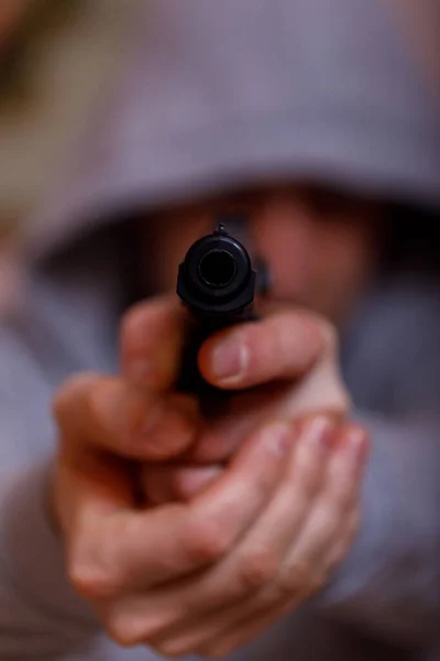Man in hood with gun or pistol. Gangster, violence, outrage, force, rape or criminal concept, focus on the gun.