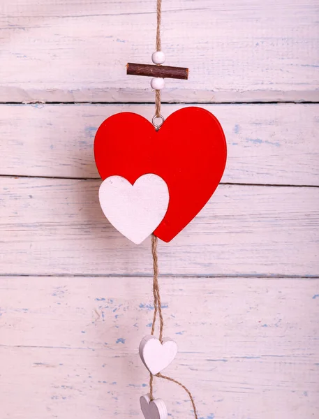 A red romantic wooden heart hanging on painted white boards. Hearts handing on the rope. Valentine\'s day greeting card. Love concept