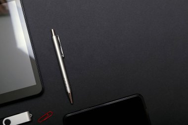 İş yeri, tablet bilgisayar ve akıllı telefon siyah masada. Siyah masadaki siyah aksesuarlar, üst görünüm