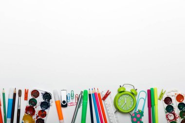 Farklı kırtasiye malzemeleri, çalar saat ve beyaz arka planda renkli malzemeler. Okul konseptine geri dönelim. Çalar saat, boya, kalem ve makas. Yukarıdan görüntüle