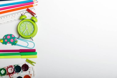 Farklı kırtasiye malzemeleri, çalar saat ve beyaz arka planda renkli malzemeler. Okul konseptine geri dönelim. Çalar saat, boya, kalem ve makas. Yukarıdan görüntüle