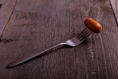 Dumanlı sosis. Çatalda kaynamış sosis ve buharın eski ahşap masa üzerindeki etkisi..