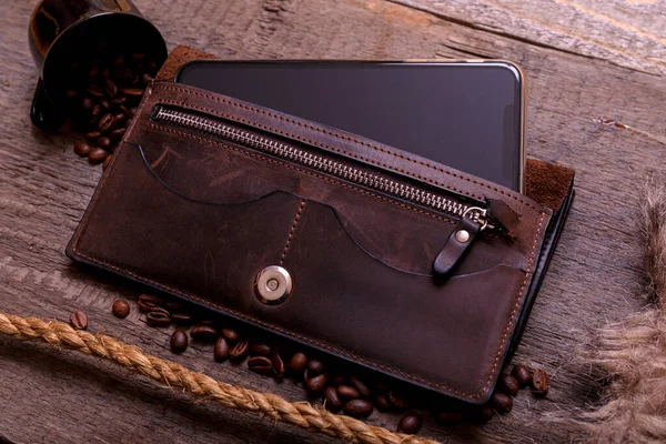 Still life photography of brown leather wallet, coffee beans, mobil phone and rope on vintage wooden background. Men casual concept, vintage and retro style.