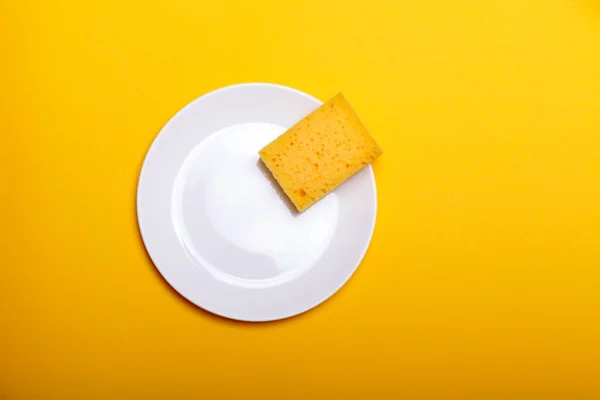 Cleaning sponge on a white plate on a yellow background
