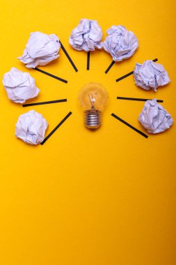 İlham konsepti buruşmuş kağıt ve iyi fikir için ampul metaforu. Beyaz buruşmuş kağıt ve sarı arka planda ampul, düz yatıyordu..