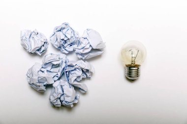 İlham konsepti buruşmuş kağıt ve iyi fikir için ampul metaforu. Beyaz arka planda beyaz buruşuk kağıt ve ampul, düz yatıyordu..