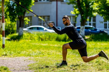 Çok çalışıyorum. Spor kıyafetli genç ve güçlü bir sporcunun parkta trx fitness kayışlarıyla şınav çekerken yan görüntüsü..