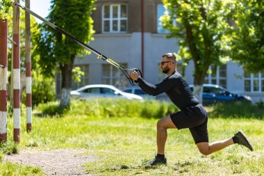 Çok çalışıyorum. Spor kıyafetli genç ve güçlü bir sporcunun parkta trx fitness kayışlarıyla şınav çekerken yan görüntüsü..