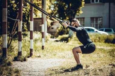 Genç çekici adam, dışarıda spor kemerleriyle süspansiyon eğitimi alıyor..
