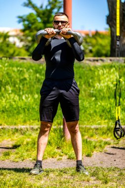 Parkın dışında kettlebell ile egzersiz yapan formda genç bir adam. Parkta sabah antrenman yapan güçlü bir genç..