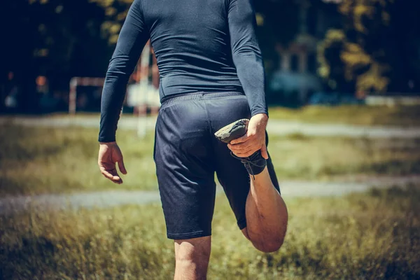 自然を背景にストレッチ筋肉の若い男の屋外イメージ 公園で足を伸ばしている スポーツ ライフスタイル 人々のコンセプト — ストック写真