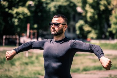 Genç adam parkta antrenman yapmadan önce esneme hareketleri yapıyor..
