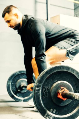 Spor kıyafetli genç bir adam spor salonunda antrenman yaparken ağırlık kaldırmaya hazırlanıyor. Fitness sporu veya sağlıklı yaşam tarzı konsepti.