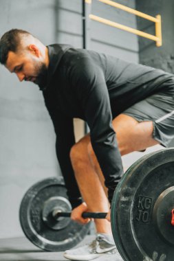 Spor kıyafetli genç bir adam spor salonunda antrenman yaparken ağırlık kaldırmaya hazırlanıyor. Fitness sporu veya sağlıklı yaşam tarzı konsepti.