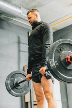 Spor kıyafetli genç bir adam spor salonunda antrenman yaparken ağırlık kaldırmaya hazırlanıyor. Fitness sporu veya sağlıklı yaşam tarzı konsepti.