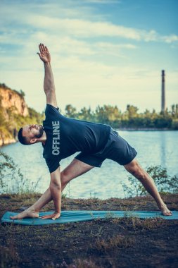 Sportif sakallı adam kayalık deniz kıyısında kol dengesi kuruyor. Taş ocağı gölünde Uluslararası Yoga Günü.