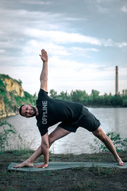 Sportif sakallı adam kayalık deniz kıyısında kol dengesi kuruyor. Taş ocağı gölünde Uluslararası Yoga Günü.