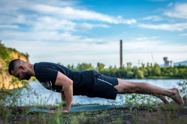 Sakallı yakışıklı yoga yapıyor ve güzel doğanın arka planında lotus pozisyonunda meditasyon yapıyor. Uluslararası yoga günü.