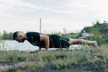 Sade, sakallı, siyah elbiseli, esneme sporu yapan, yoga yapan, spor yapan, spor yapan, spor yapan, spor yapan veya yeşil çimenlikte egzersiz yapan, esnek omurga egzersizi yapan çekici bir genç profili..