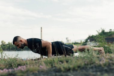 Sade, sakallı, siyah elbiseli, esneme sporu yapan, yoga yapan, spor yapan, spor yapan, spor yapan, spor yapan veya yeşil çimenlikte egzersiz yapan, esnek omurga egzersizi yapan çekici bir genç profili..