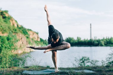 Taş ocağı gölünde yoga yapan yakışıklı, sakallı bir adam. Uluslararası Yoga Günü konsepti.