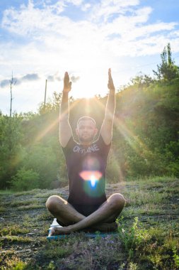 Mükemmel vücut adamının silueti günbatımı arka planında kayanın üzerinde yoga yapıyor. Uluslararası Yoga Günü.