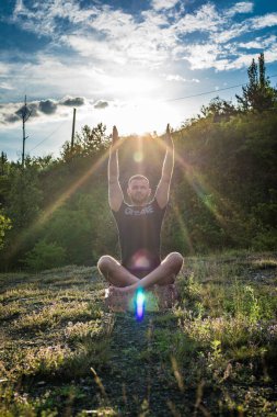 Mükemmel vücut adamının silueti günbatımı arka planında kayanın üzerinde yoga yapıyor. Uluslararası Yoga Günü.