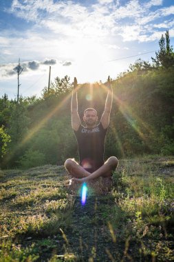 Mükemmel vücut adamının silueti günbatımı arka planında kayanın üzerinde yoga yapıyor. Uluslararası Yoga Günü.