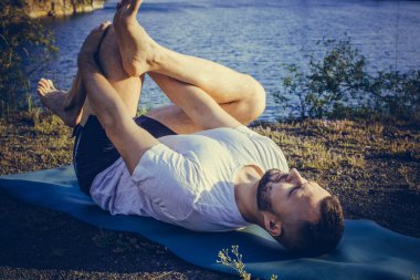 Genç sakallı adam yoga yapıyor ve Asana 'da duruyor. Güzel dağ taş ocağı gölü manzarası. Karmaşık ve komik yoga filmi. Uluslararası Yoga Günü