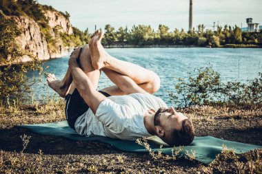 Genç sakallı adam yoga yapıyor ve Asana 'da duruyor. Güzel dağ taş ocağı gölü manzarası. Karmaşık ve komik yoga filmi. Uluslararası Yoga Günü