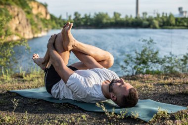 Genç sakallı adam yoga yapıyor ve Asana 'da duruyor. Güzel dağ taş ocağı gölü manzarası. Karmaşık ve komik yoga filmi. Uluslararası Yoga Günü